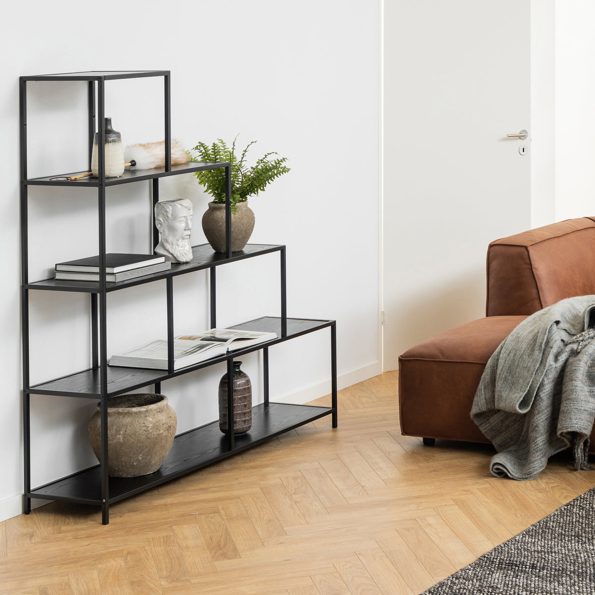 Regał Skeleto 135x150 Czarna Melamina w salonie obok brązowej sofy, z rośliną, popiersiem i książkami